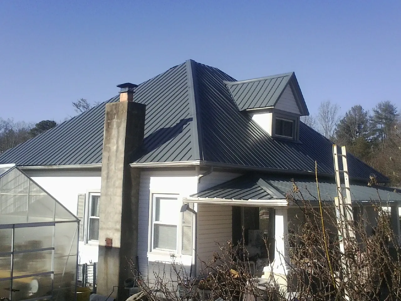 Dark blue standing seam metal roof on a white farmhouse with dormer — Slate & Tile Roof Repair by Roofing Brothers in Henry