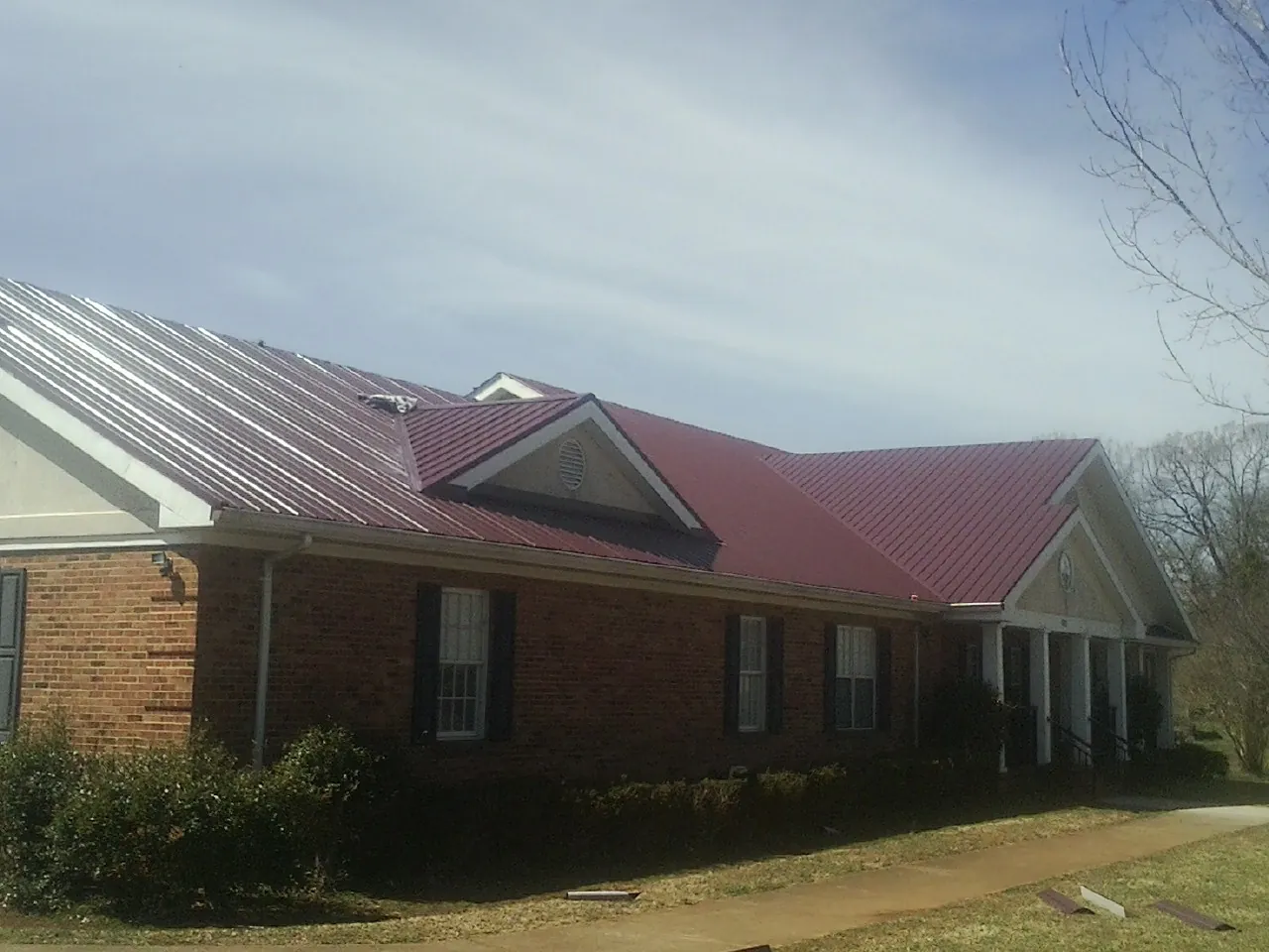 Red metal roof with gabled entries on a long brick building, from a Hail Damage Roof Repair job in Henry