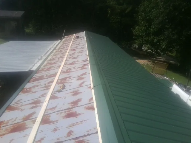 Old rusted panels beside newly installed green metal roofing — Wind Damage Roof Repair by Roofing Brothers in Henry
