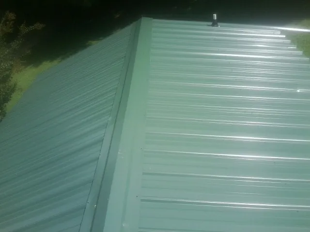 New green metal panels meeting at the ridge of a roof — Flat Roof Repair work by our crew in Henry