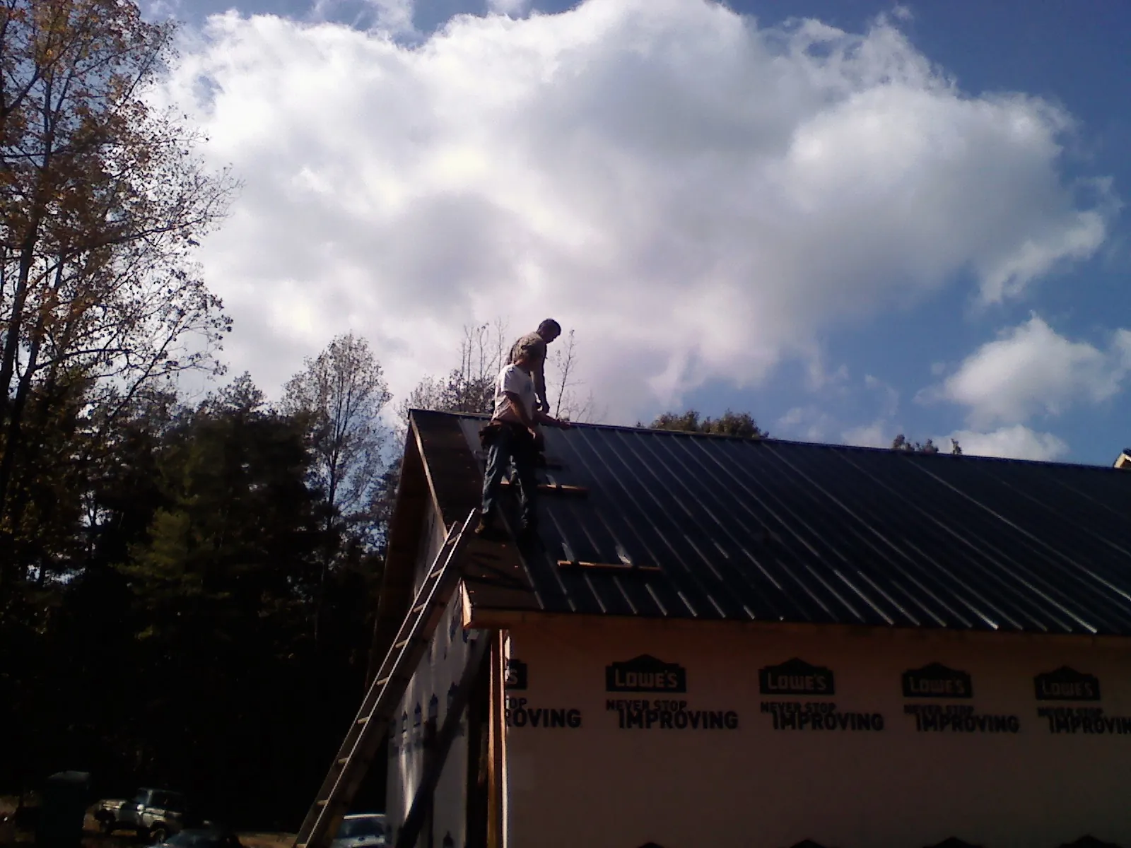 Roofer fastening dark metal panels high against a cloudy sky, from a Roof Inspection job in Henry