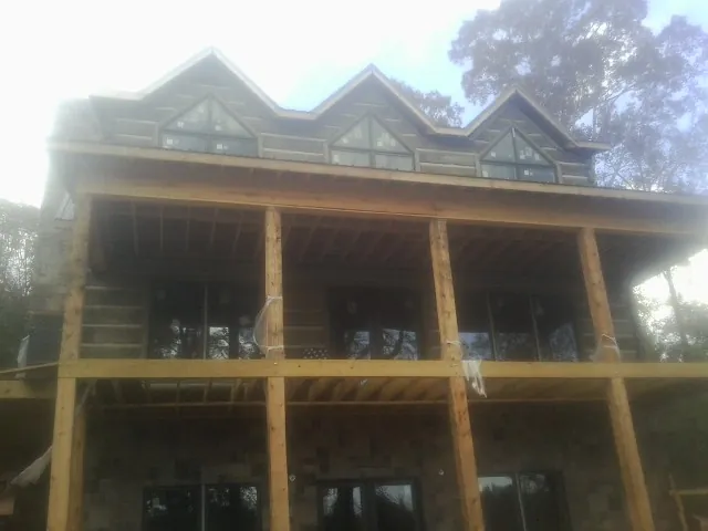 Dormers and porch framing on a large log home under construction — Roof Coating work by our crew in Henry
