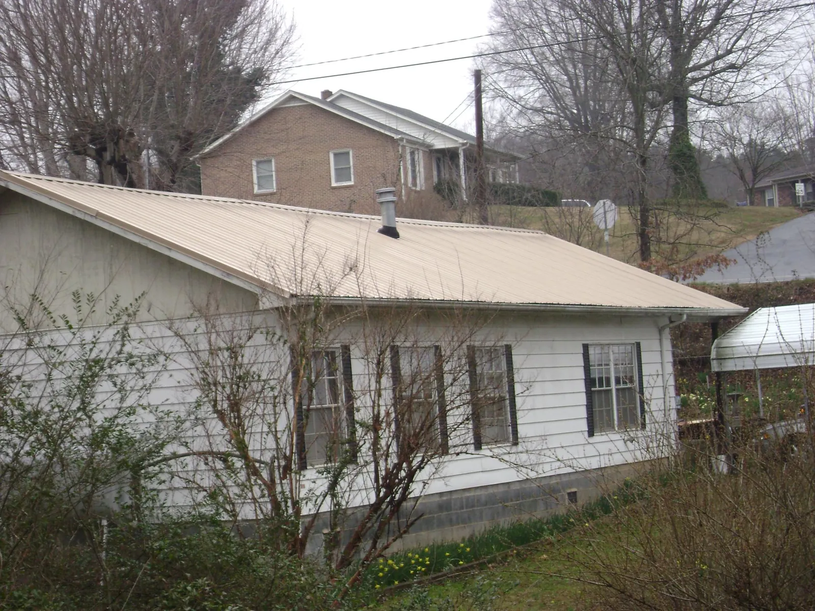Tan metal roof on a white sided house set into a hillside — Commercial Roofing by Roofing Brothers in Henry