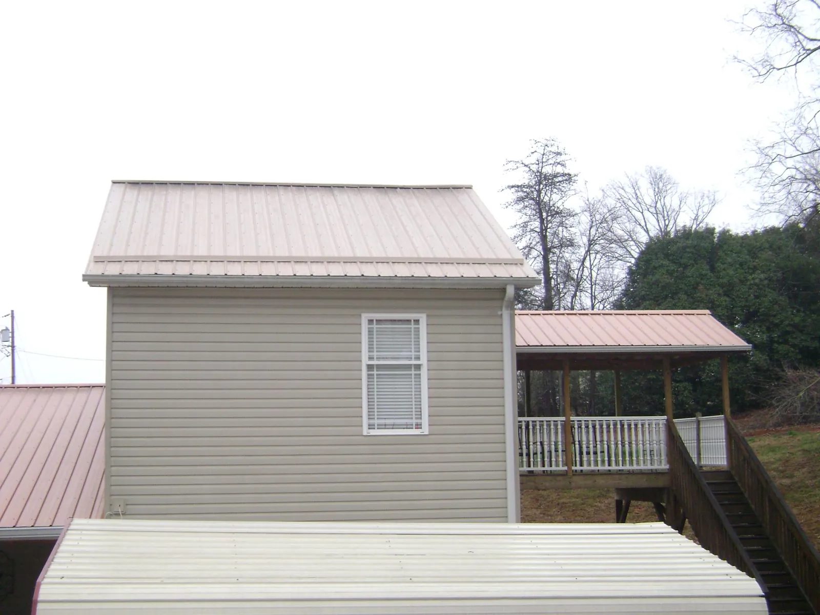 Tan metal roofs on a two story addition and attached porch, from a Roof Replacement job in Henry